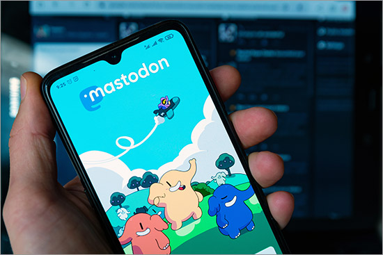 Mastodon art showing three different colored dancing elephants (yellow, orange and blue) waving at a plane pilot zig zagging across the sky is seen an the login page of the Mastodon app on an iPhone. Mastodon, a decentralized platform, rapidly gains users after Elon Musk's Twitter takeover.