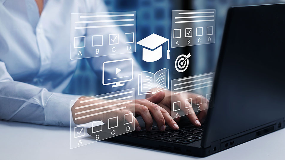 A person in a light blue dress shirt is typing on a black laptop, with digital education-themed graphics overlaid in the foreground, including icons of a graduation cap, open book, computer screen with a play button, target, and multiple-choice answer boxes labeled A to D; the image suggests online learning, e-learning platforms, or digital exams in a modern, tech-enabled environment.