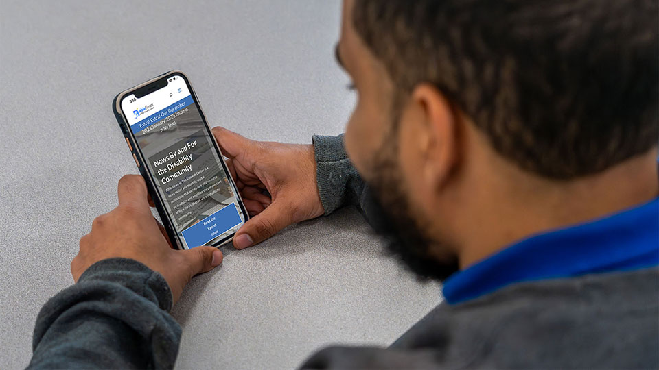 Male with dark brown hair and beard, wearing a blue shirt, reading Able News on his cellphone.
